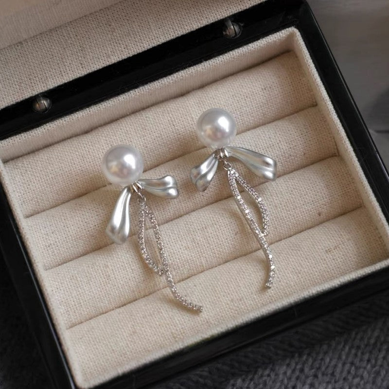 花のリボンの弓形のジルコンのイヤリングを持っている