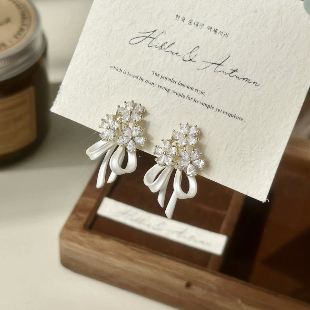 花のリボンの弓形のジルコンのイヤリングを持っている