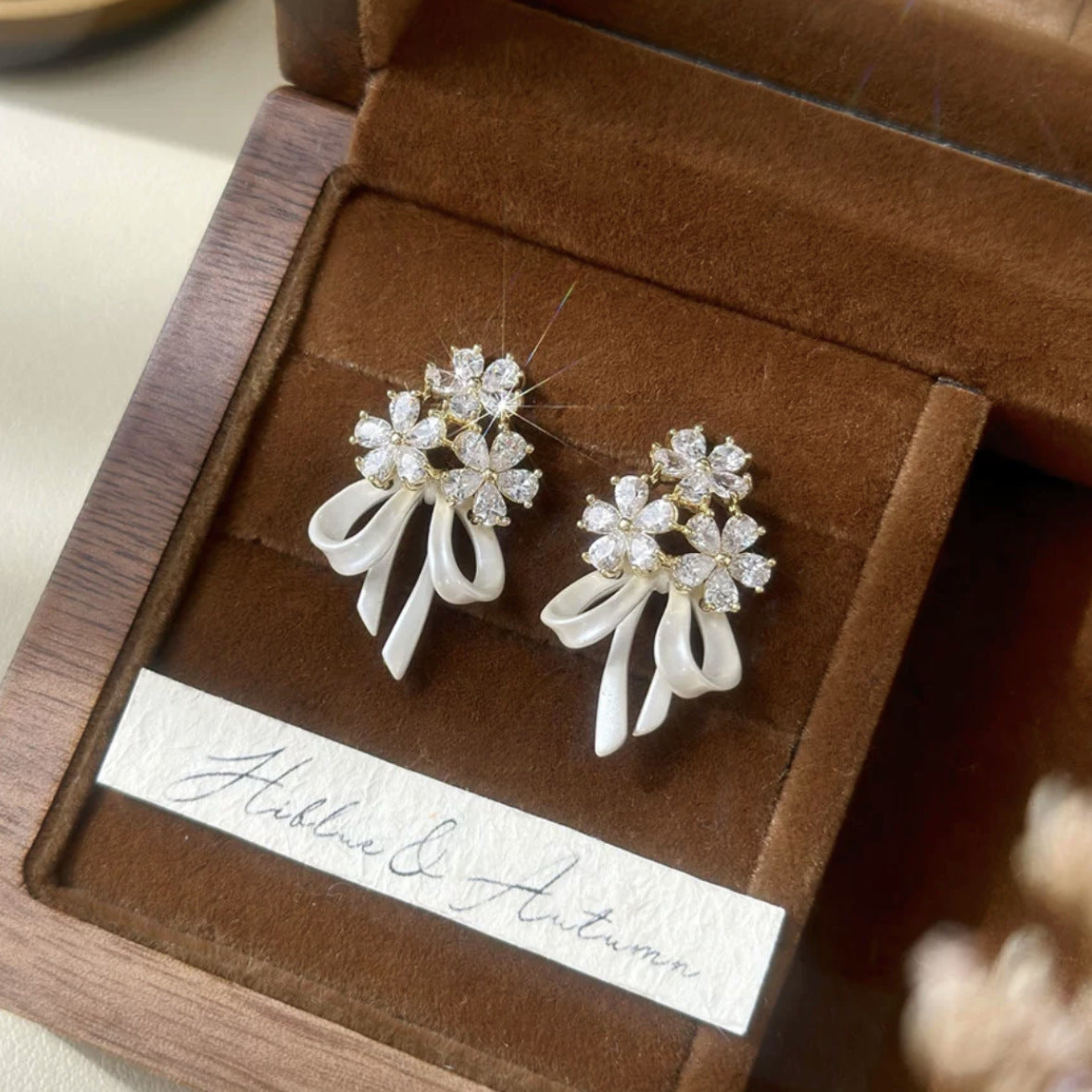 花のリボンの弓形のジルコンのイヤリングを持っている